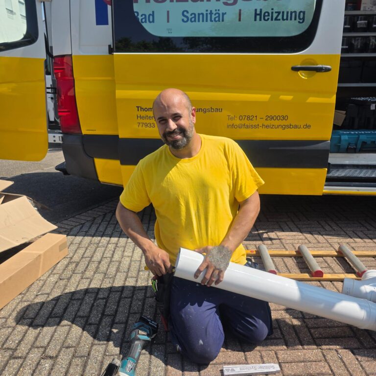 Ein Mann in einem gelben Hemd kniet auf dem Boden, hält ein weißes Rohr in der Hand und legt Werkzeug daneben, vor einem gelben Servicewagen an einem sonnigen Tag - eine ideale Szene für eine "über uns"-Einführung.